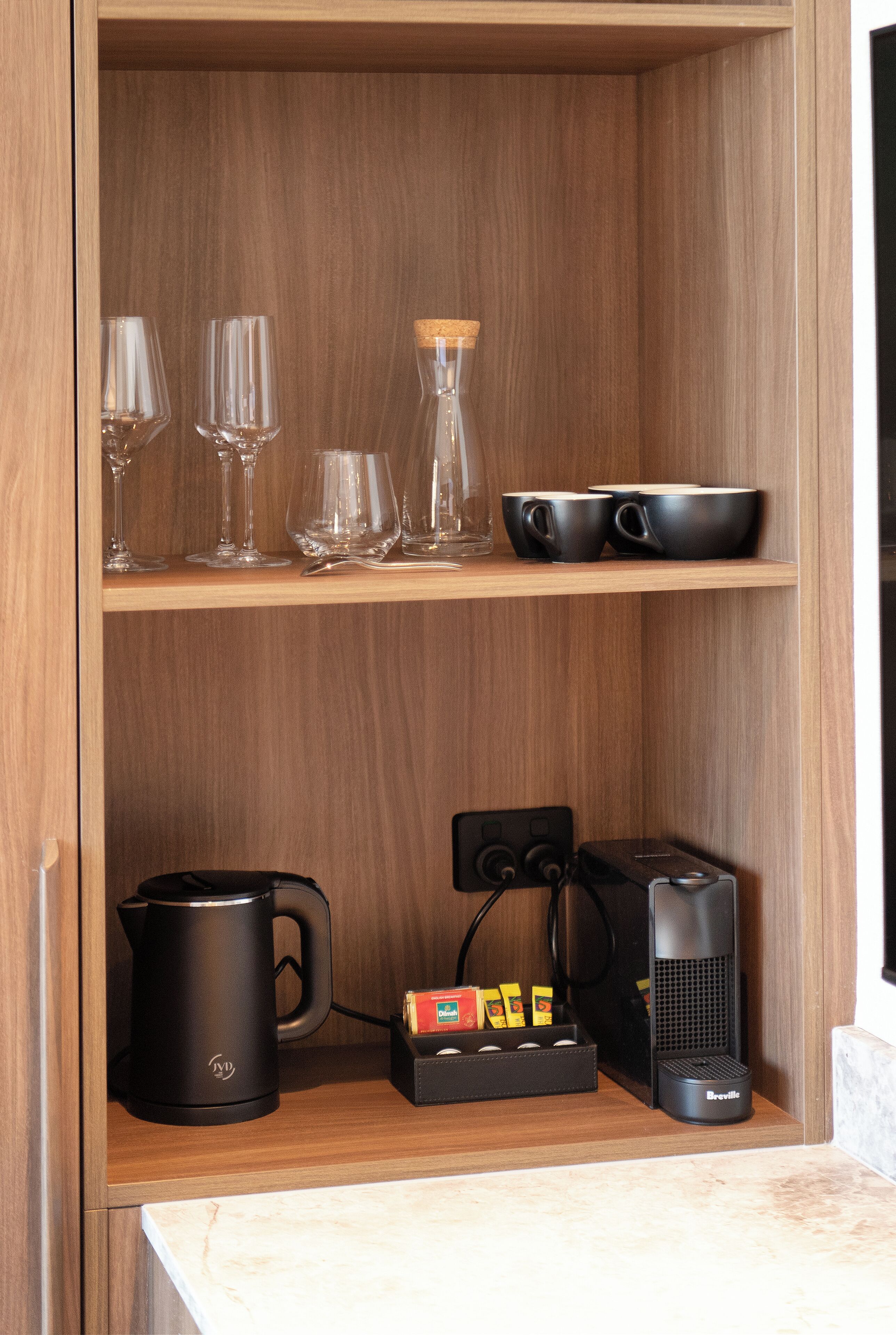A wooden shelf with glassware and a coffee maker.