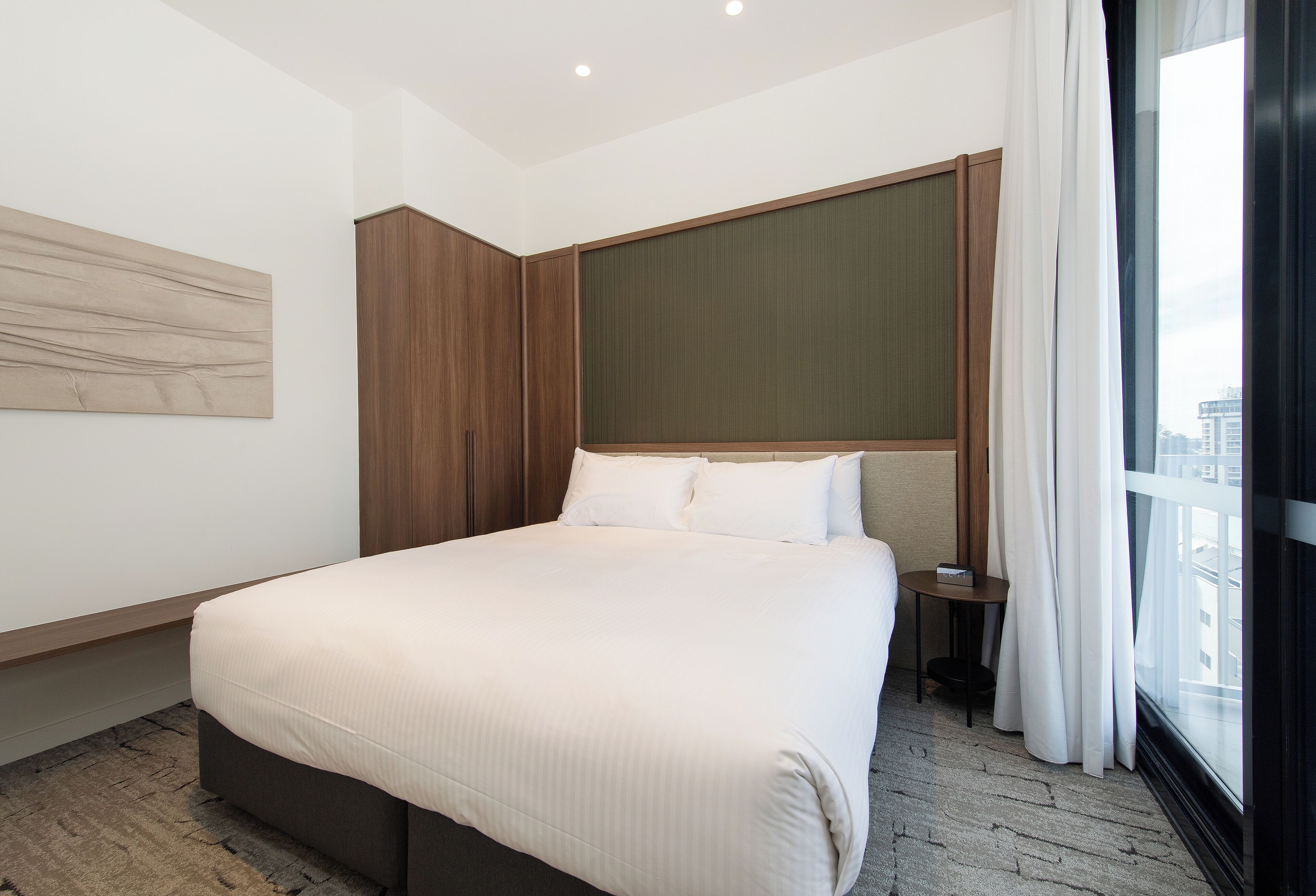 Een moderne hotelkamer met een groot bed, een houten kledingkast, een klein nachtkastje en een raam met gordijnen.