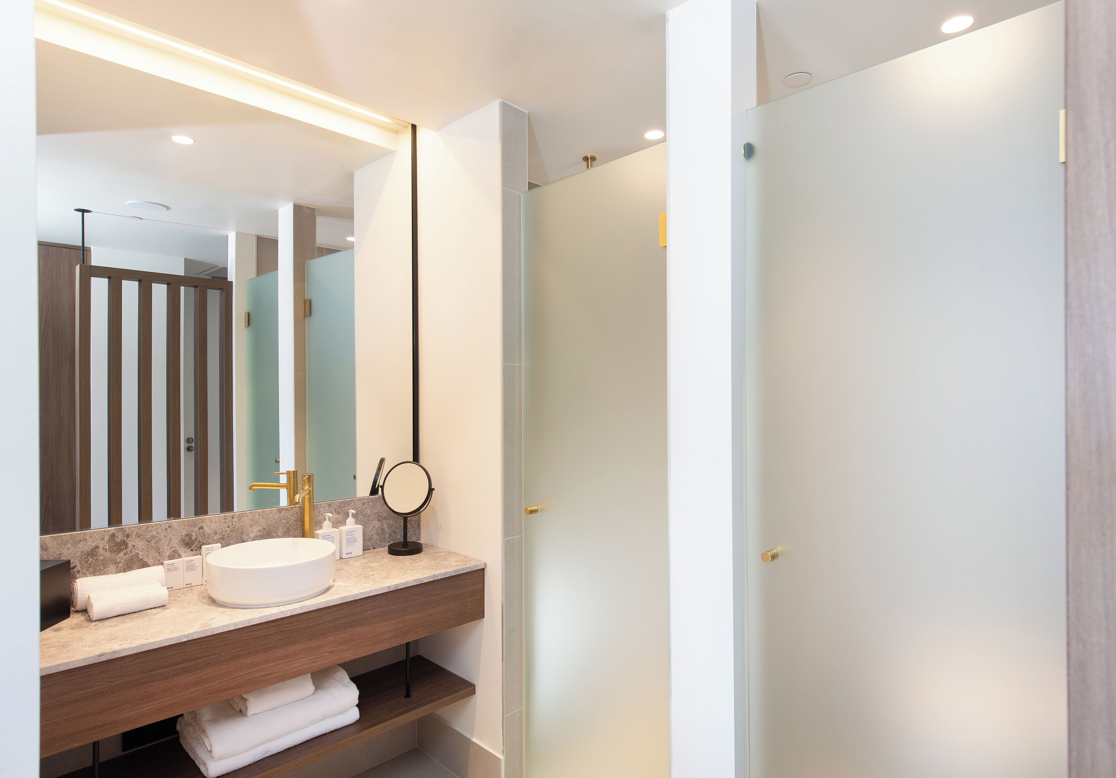 A modern bathroom with a large mirror, a round sink, and a glass shower enclosure.