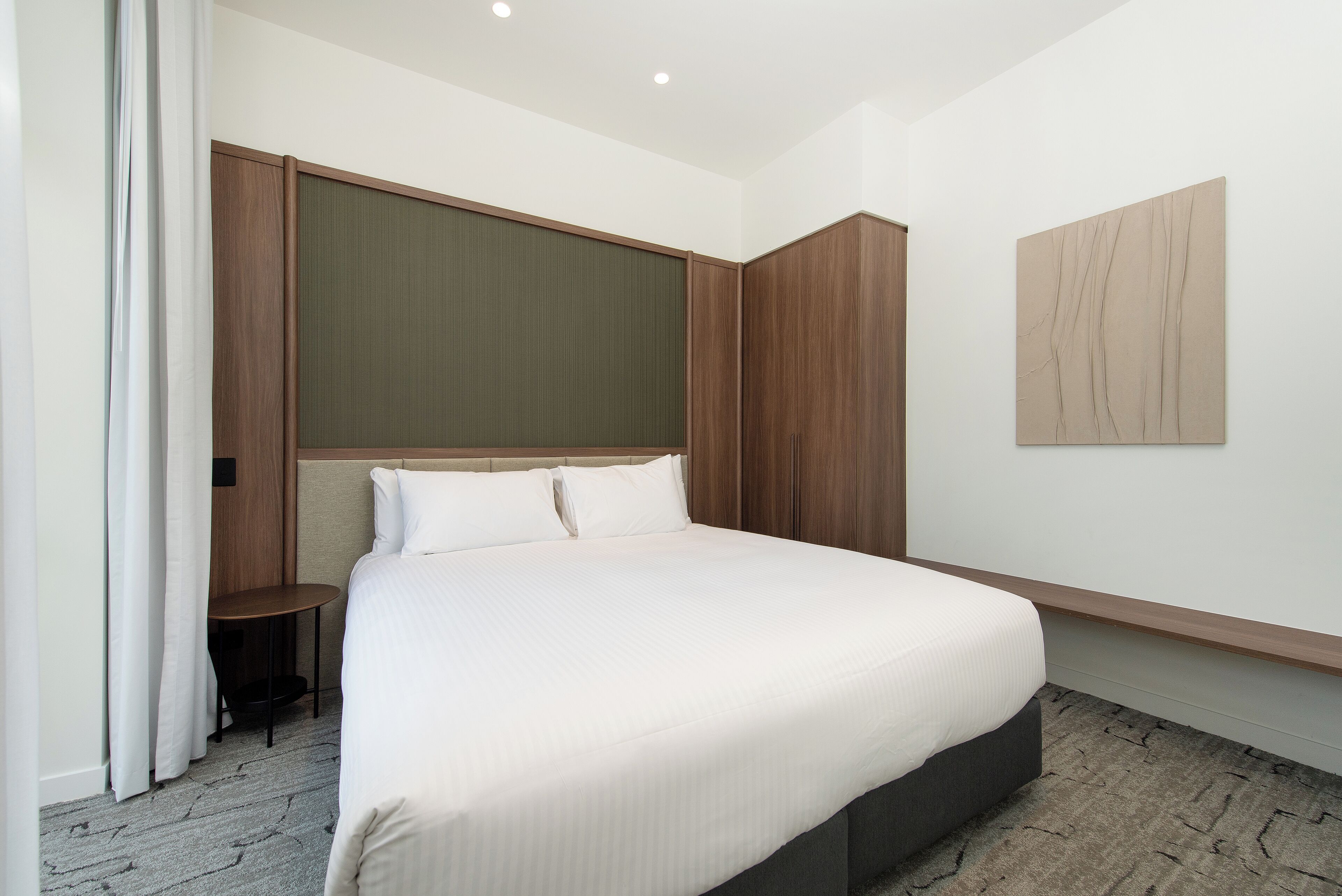 Een moderne hotelkamer met een groot bed, een kleine tafel en een kast.