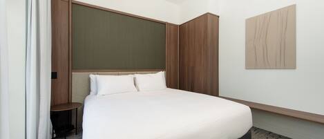Een moderne hotelkamer met een groot bed, een kleine tafel en een kast.