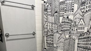 A bathroom with a white toilet, a shower curtain with a cityscape design, and a tiled floor with hexagonal patterns. - Charming 2-bedroom apartment with wifi.   Three blocks to ferry.   (New Orleans)