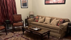 A living room with a patterned rug, a sofa, a coffee table, and a chair. There are two framed pictures on the wall. - Charming 2-bedroom apartment with wifi.   Three blocks to ferry.   (New Orleans)