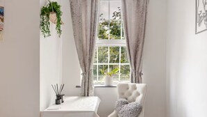 A room with a white chair, a small table, and a window with curtains.