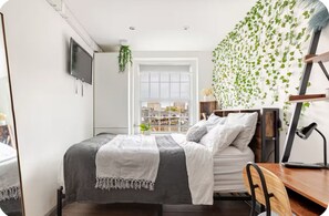 Une chambre à coucher comprenant un lit, un bureau, une chaise et une fenêtre donnant sur la ville.