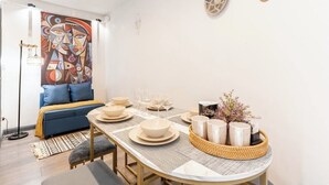 A modern dining area with a round table set for four, a blue sofa, and a colorful abstract painting on the wall.