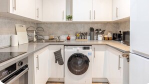 A modern kitchen with white cabinets, a built-in washing machine, a microwave, and a coffee maker.