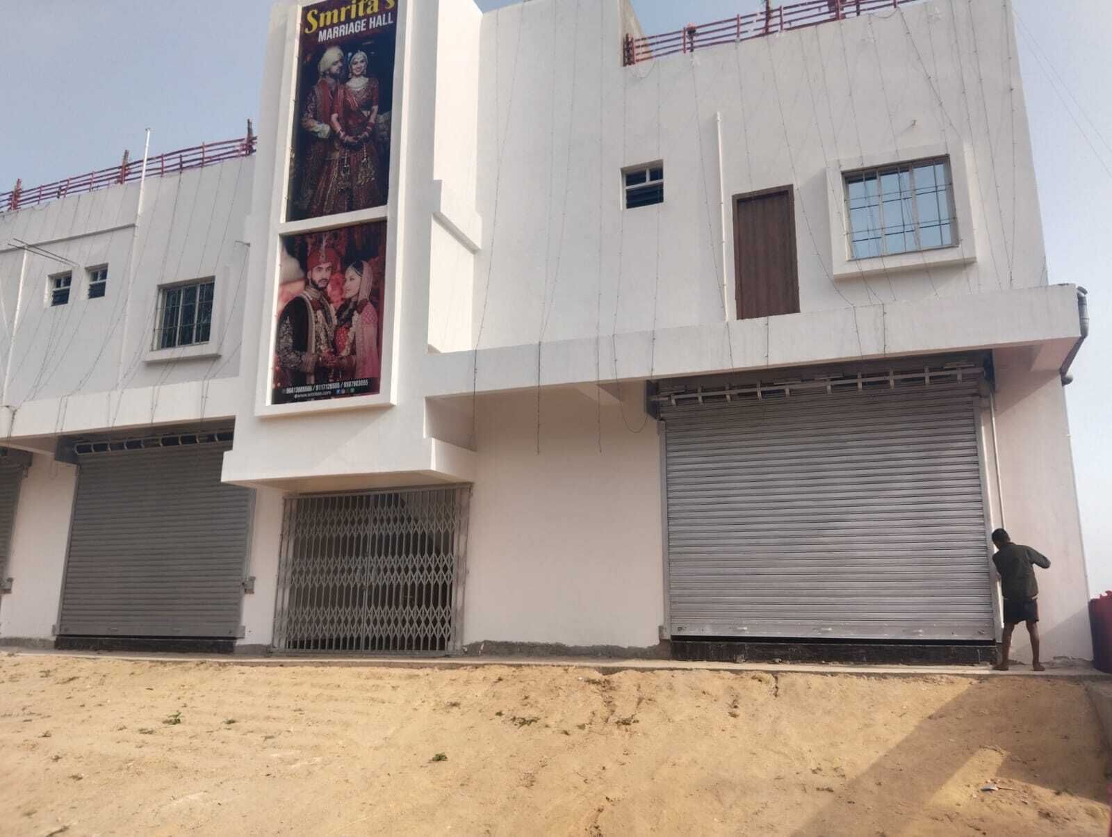 A building with two closed shuttered entrances, a poster advertising a marriage hall, and a person standing near the right shutter.