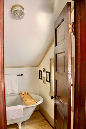 Une salle de bain avec une baignoire blanche, un abattant de toilettes en bois et une porte en bois.