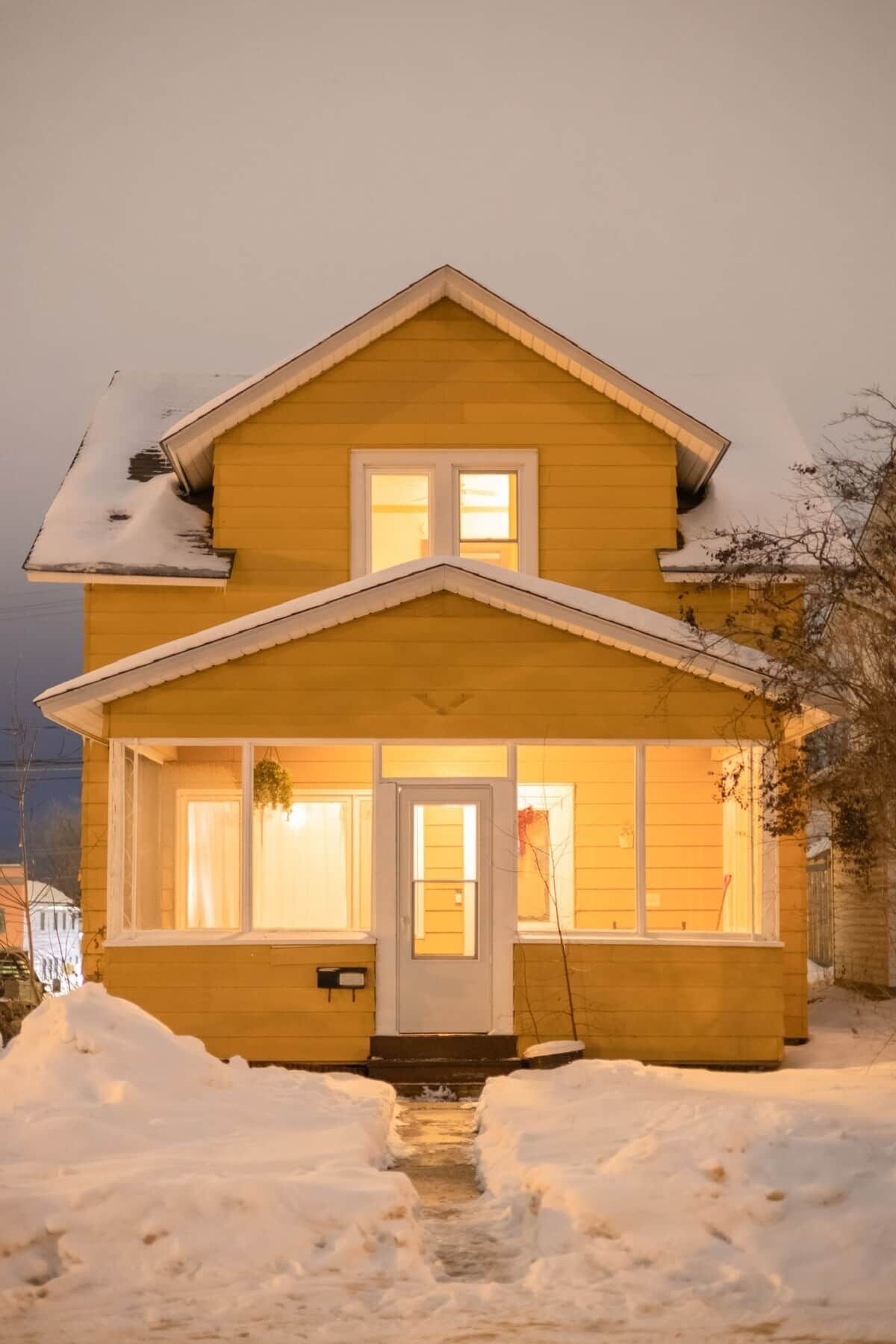 A two-story house with a front door, windows, and a snow-covered ground.