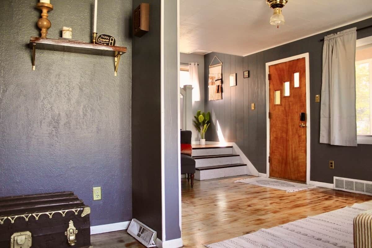 A hallway with a wooden door, a staircase, and a coat rack with a sign.