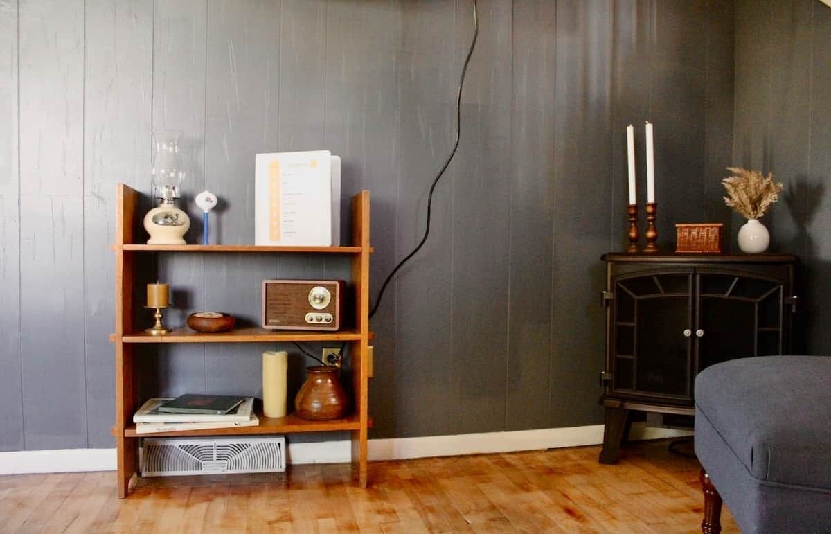 A room with a wooden bookshelf, a vintage radio, a candle, and a small cabinet with candles.