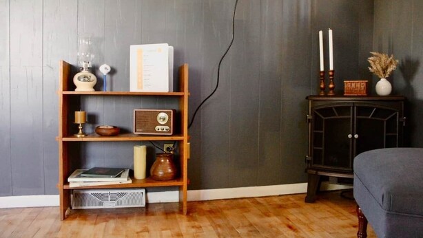 Ein Zimmer mit einem hölzernen Bücherregal, einem alten Radio, einer Kerze und einem kleinen Schrank mit Kerzen.