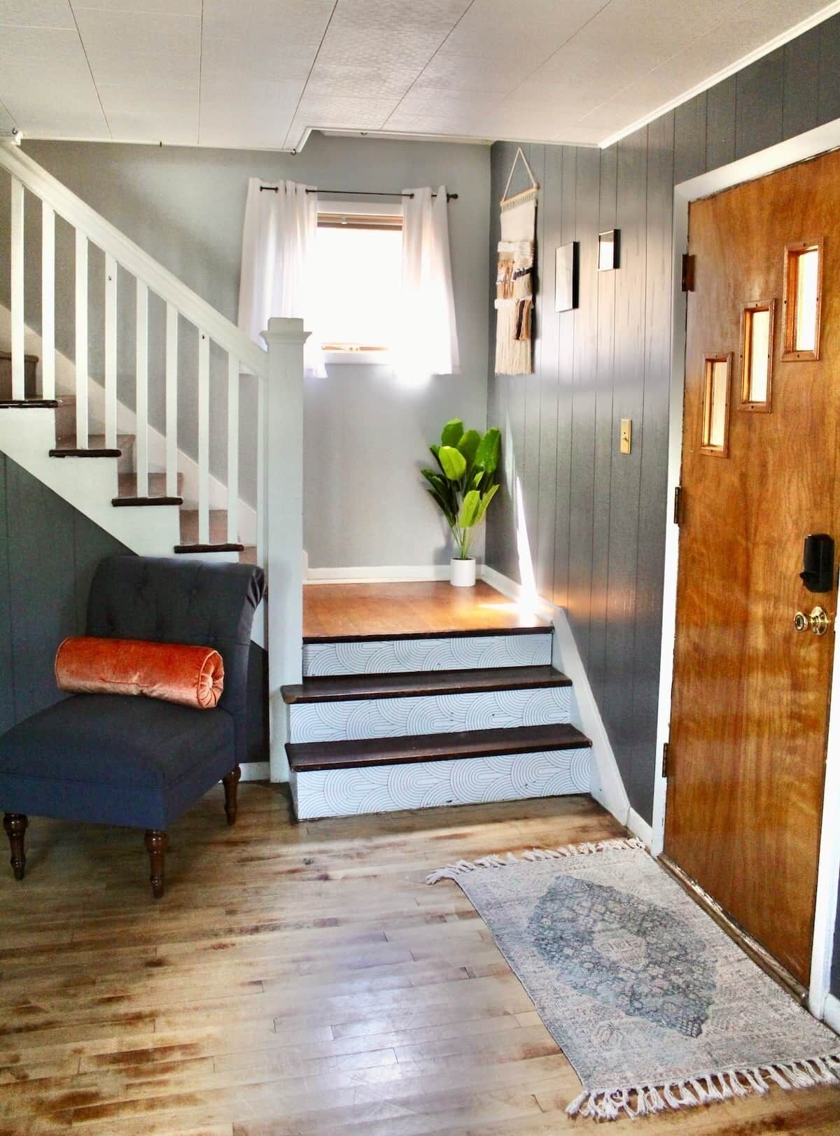 Una escalera conduce a una plataforma con una planta, una silla y una puerta de madera.