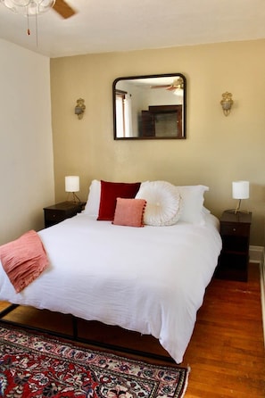 A neatly arranged bedroom with a bed, bedside tables, a mirror, and a patterned rug.
