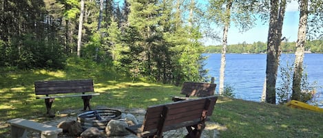 A lakeside park with a wooden bench, a concrete bench, and a fire pit.