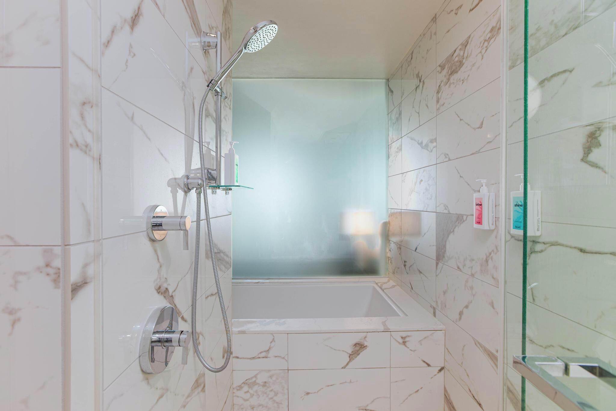 A modern bathroom with a glass-enclosed shower, a bathtub, and marble tiles.