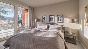 A bedroom with a large bed, a nightstand, a lamp, and a window with a view of a brick building. - Seaside 74 - Seaside 74, tastefully furnished, bright 2-room apartment with (Timmendorfer Strand)