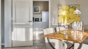 A dining area with a wooden table, white chairs, and a painting of lemons on the wall. - Seaside 74 - Seaside 74, tastefully furnished, bright 2-room apartment with (Timmendorfer Strand)