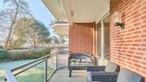 A balcony with wicker furniture, a glass railing, and a brick wall. - Seaside 74 - Seaside 74, tastefully furnished, bright 2-room apartment with (Timmendorfer Strand)