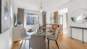 A modern dining area with a round table, grey chairs, and a glass chandelier.
