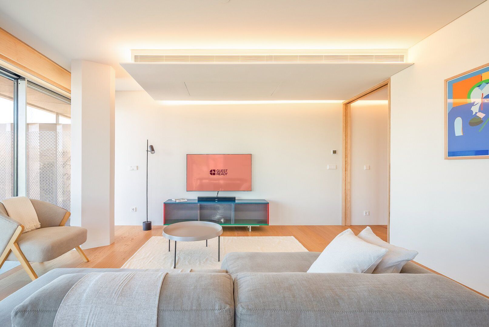 Un salon moderne avec un canapé gris, une petite table ronde et un téléviseur à écran plat posé sur un meuble.