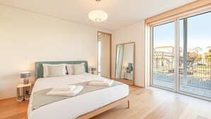 Un dormitorio moderno con una cama grande, lámparas de noche, un espejo y un balcón con vistas a la ciudad.