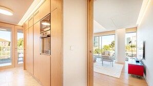 Una cocina moderna con electrodomésticos integrados, un comedor con un detalle rojo y ventanas grandes que ofrecen vistas al exterior.