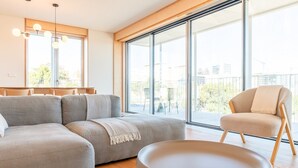 Una sala de estar moderna con un sofá modular, una mesa de centro redonda y una silla. Amplias ventanas ofrecen vistas de la ciudad.