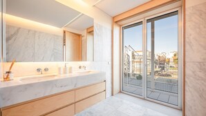 Un baño moderno con un espejo grande, lavamanos doble y vistas a la ciudad a través de una puerta corredera de vidrio.