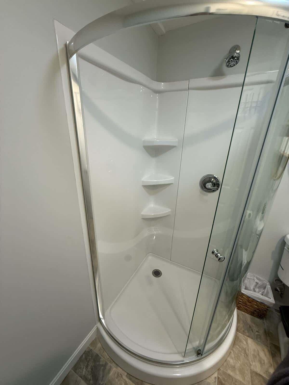 Une cabine de douche en verre avec un design d’angle, une pomme de douche en acier inoxydable et un seul bouton de commande.
