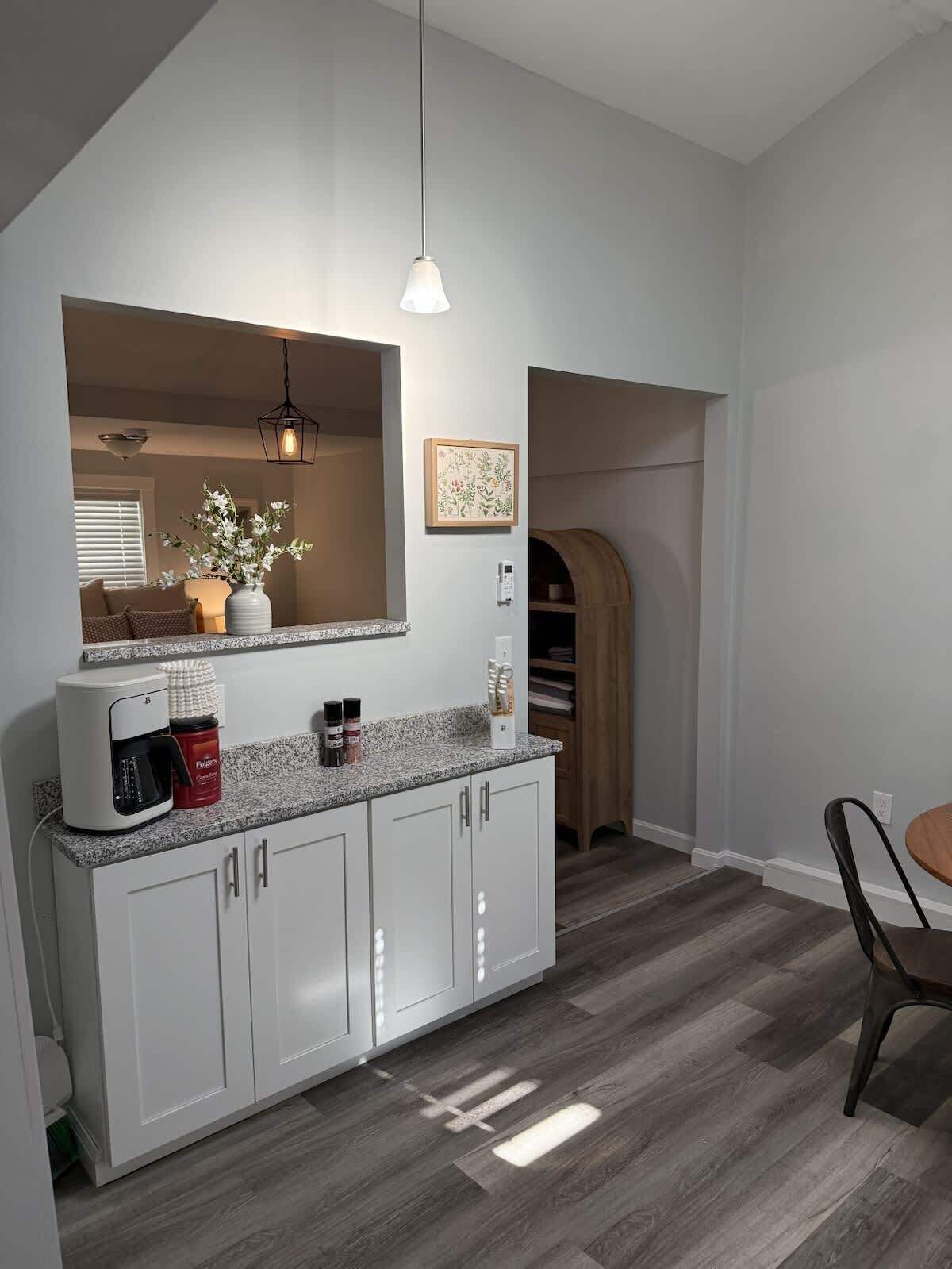 Une cuisine moderne avec des meubles blancs, une machine à café et un luminaire suspendu.
