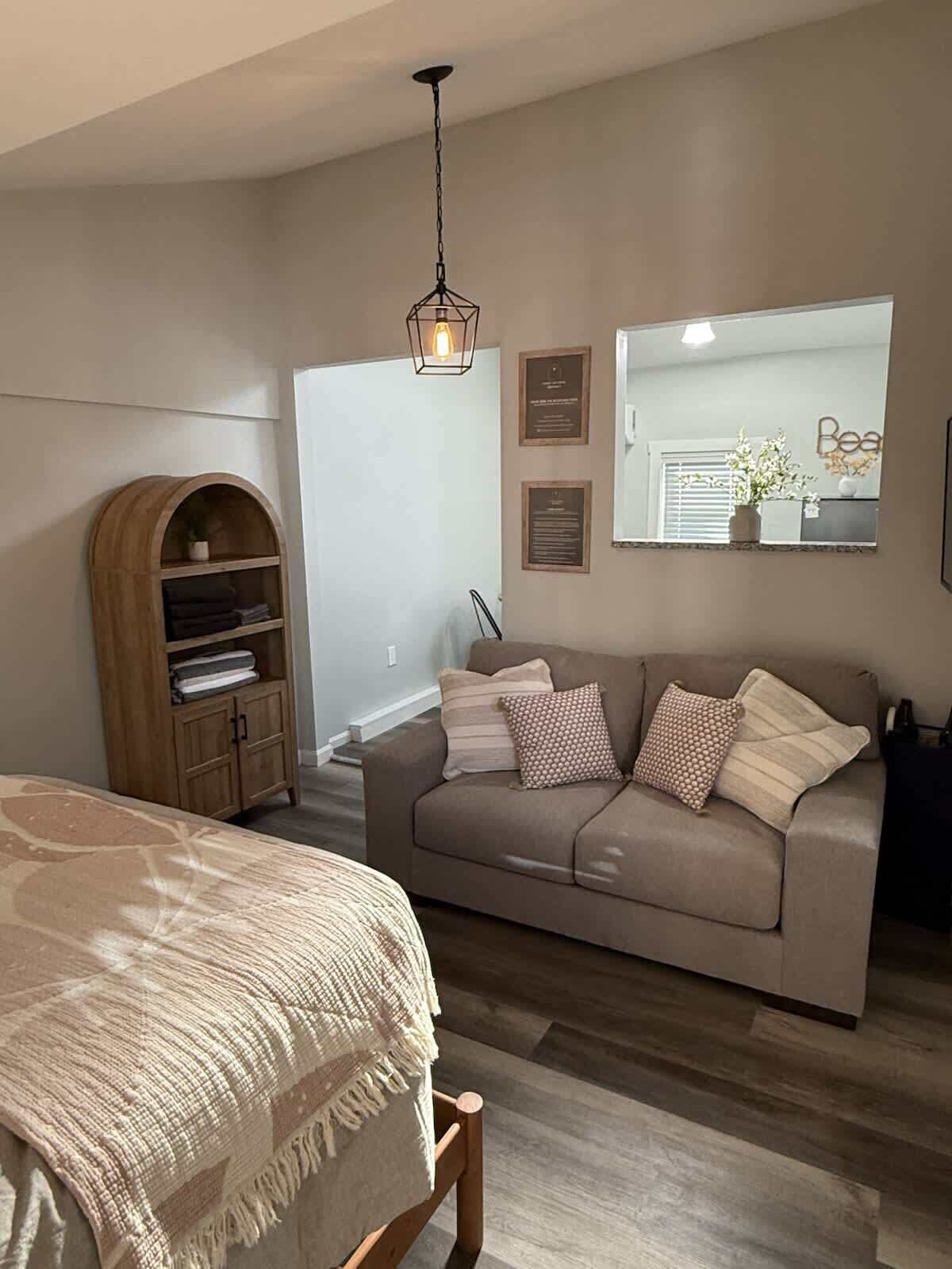 Une chambre à coucher comprenant un lit, un canapé, une armoire en bois, un luminaire suspendu et une fenêtre avec des stores.