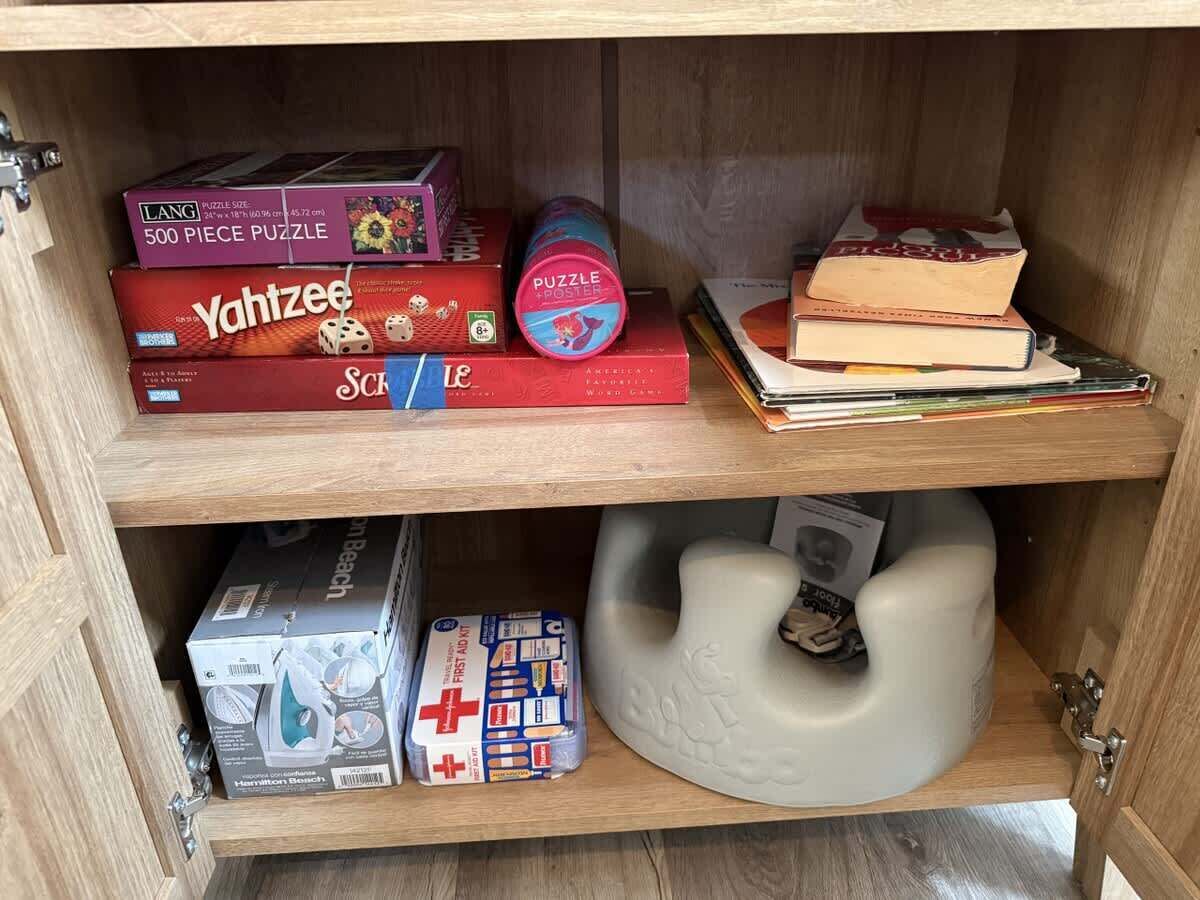 A wooden cabinet with shelves containing various items including puzzle boxes, books, a first aid kit, and a white object.