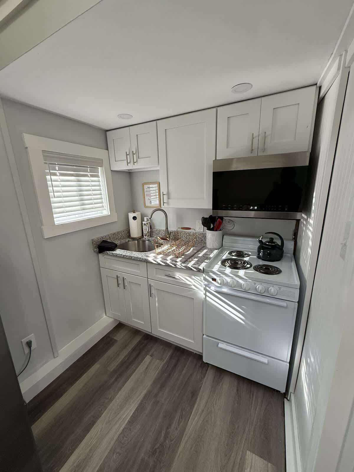 A compact kitchen with white cabinets, a stove, and a window with blinds.