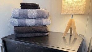 Une commode noire sur laquelle sont pliées plusieurs couvertures, une lampe en bois et un luminaire fixé au mur.