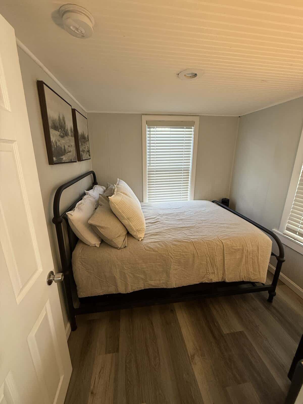 Een slaapkamer met een bed, een raam met zonwering, een deur en een plafondlamp.