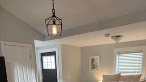 A bedroom with a bed, a bedside table, a chair, a door, and a hanging light fixture. - Driftwood Getaway - Perfect Location Near Beach! (Hampton)