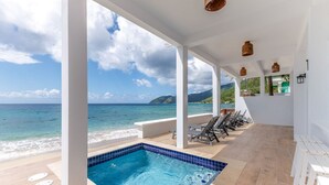 A pool area with a view of the ocean, lounge chairs, and a tiled pool.