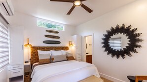 A bedroom with a bed, a ceiling fan, a wall-mounted mirror, and a window.