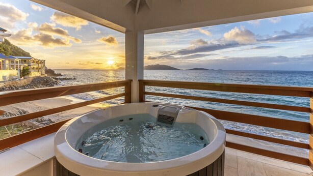 A hot tub on a balcony with a view of the sea and a building in the background.