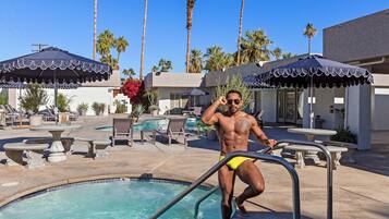 A man in swim trunks by a pool with lounge chairs and umbrellas.