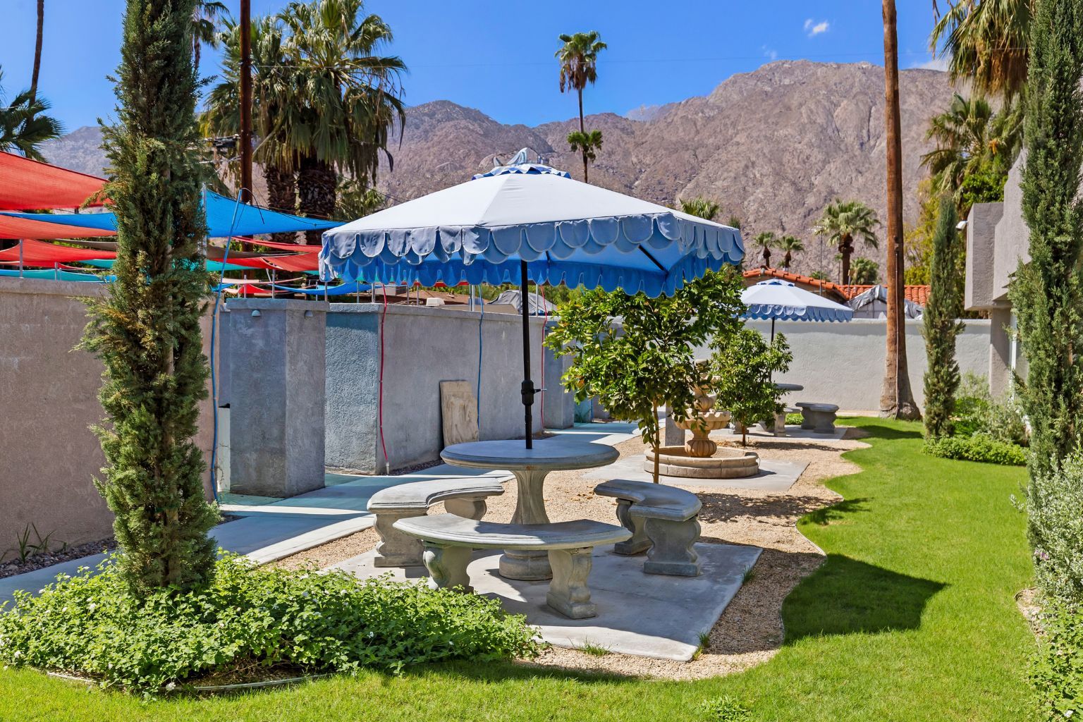 A patio area with a blue umbrella, stone tables, and a small tree.