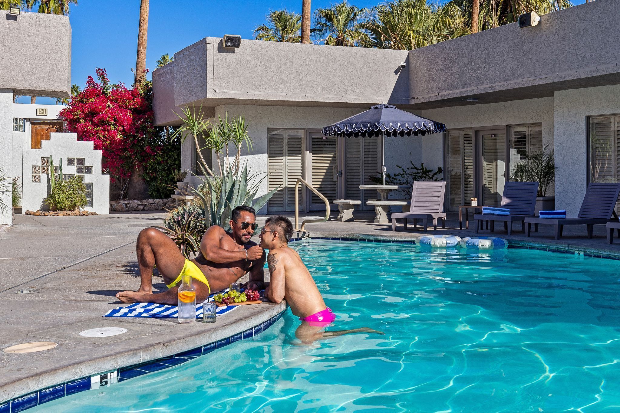 A pool area with a clear blue pool, lounge chairs, and a small table with a blue umbrella.