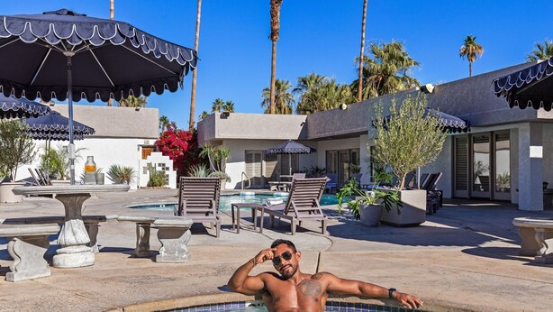 Un hombre descansando en una piscina con sillones y sombrillas alrededor.