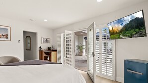 Un dormitorio con cama, televisor montado en la pared, armario y puerta que da a un balcón.