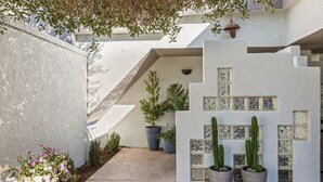 Un patio con pared de estuco blanco, plantas en macetas y piso de baldosas.