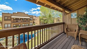 Terraza de madera con mobiliario de mimbre que da a una piscina y edificios.