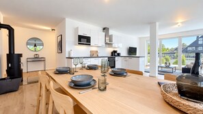 A modern kitchen with white cabinets, a black microwave, and a dining area with a wooden table set for four. - Vacation apartment in the mountain resort 3.3.5 - Adventure & wellness with infrared cabin! (Winterberg)