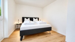 A single bed with a black frame and white bedding, a bedside table with a lamp, and a window with blinds. - Vacation apartment in the mountain resort 3.3.5 - Adventure & wellness with infrared cabin! (Winterberg)